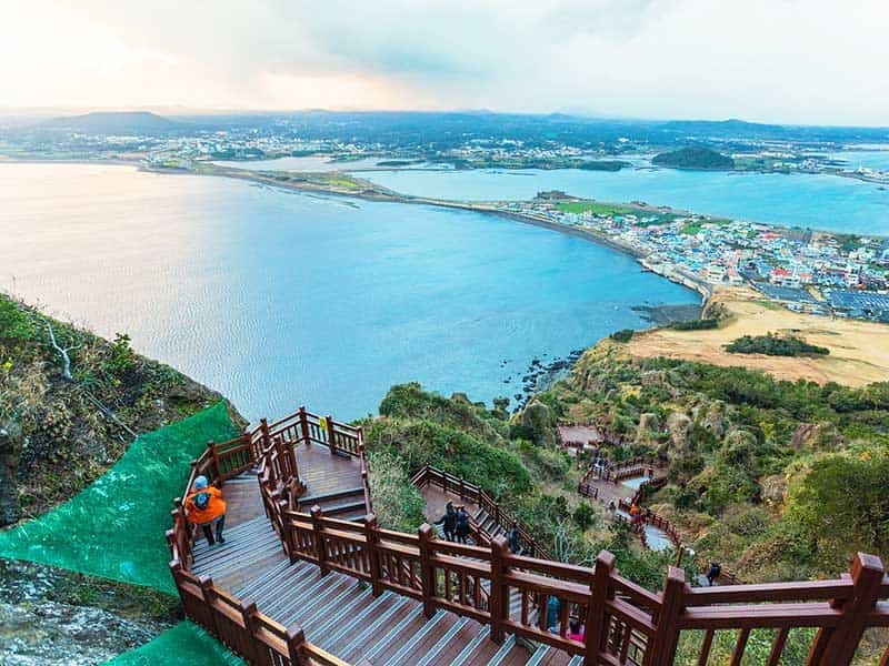 Bậc thang bằng gỗ dẫn xuống một khu vực ven biển nhìn ra Vịnh Jeju, Hàn Quốc, với làn nước xanh trong.