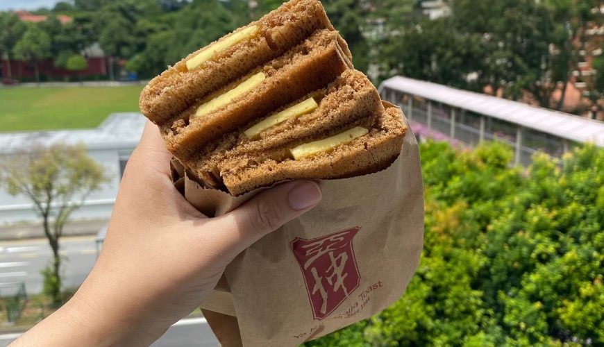 Bánh mì nâu kẹp bơ và mứt Kaya, được cầm trên tay.