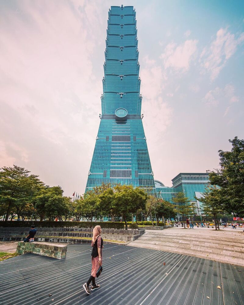 Toàn cảnh tòa nhà chọc trời Taipei 101 màu xanh ngọc bích, đứng sừng sững giữa khu vực công viên và quảng trường hiện đại.