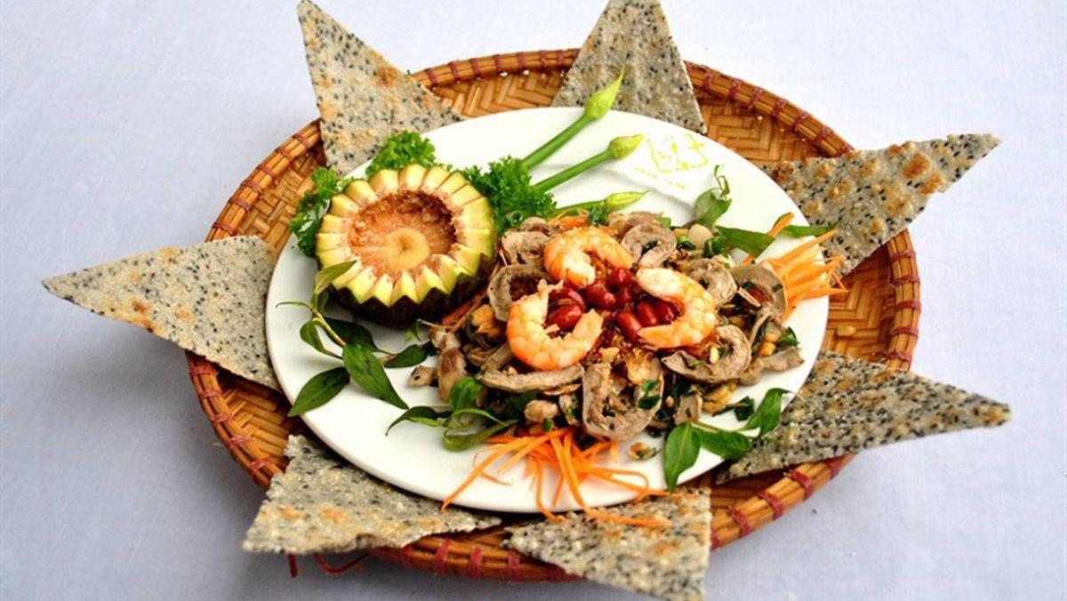 Món Vả Trộn Tôm Thịt được bày biện cầu kỳ trên đĩa trắng, ăn kèm với bánh đa mè đen.