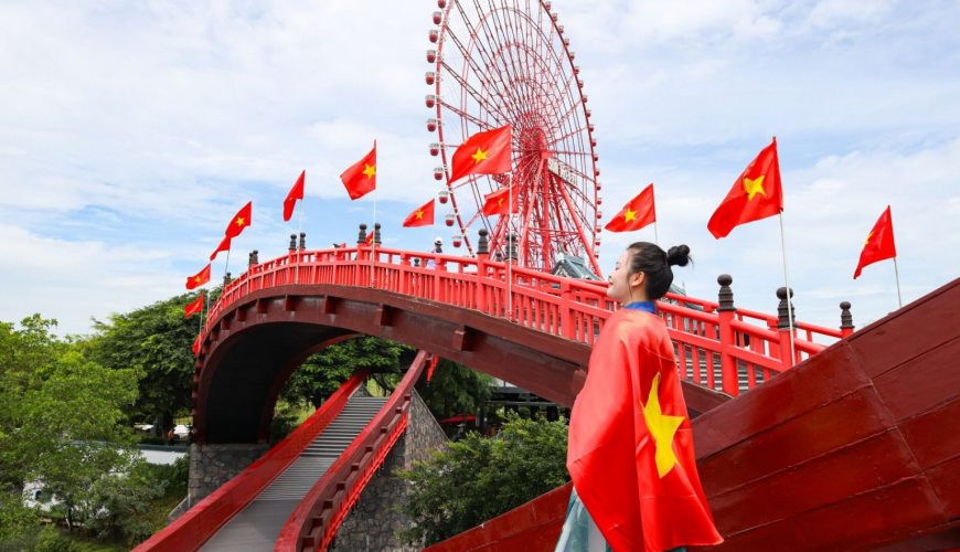 Cô gái mặc áo dài và cờ Việt Nam, đứng trên cầu đỏ với vòng quay khổng lồ